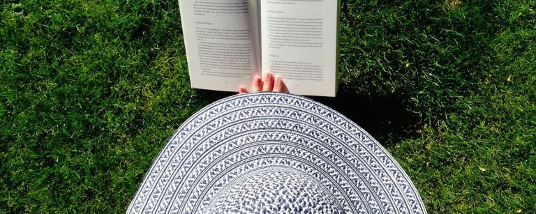 Frau mit Hut liest Buch im Gras. Perfekt für gesunde Ernährung und Fitness.