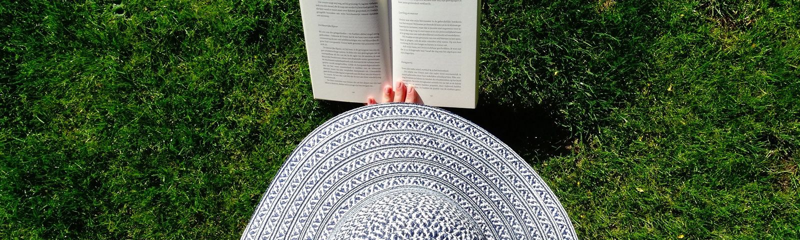 Frau mit Hut liest Buch im Gras. Perfekt für gesunde Ernährung und Fitness.