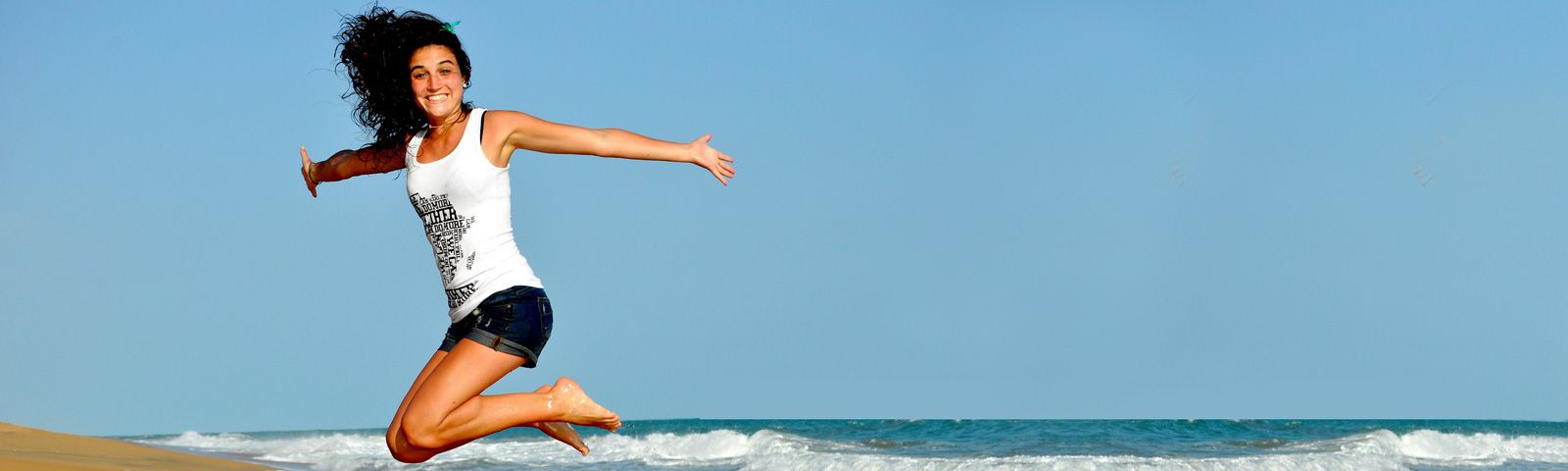 1707-hoe-ongezond-leven-we-in-de-toekomst Frau springt vor Freude am Strand, inspiriert von gesunder Ernährung und Fitness.