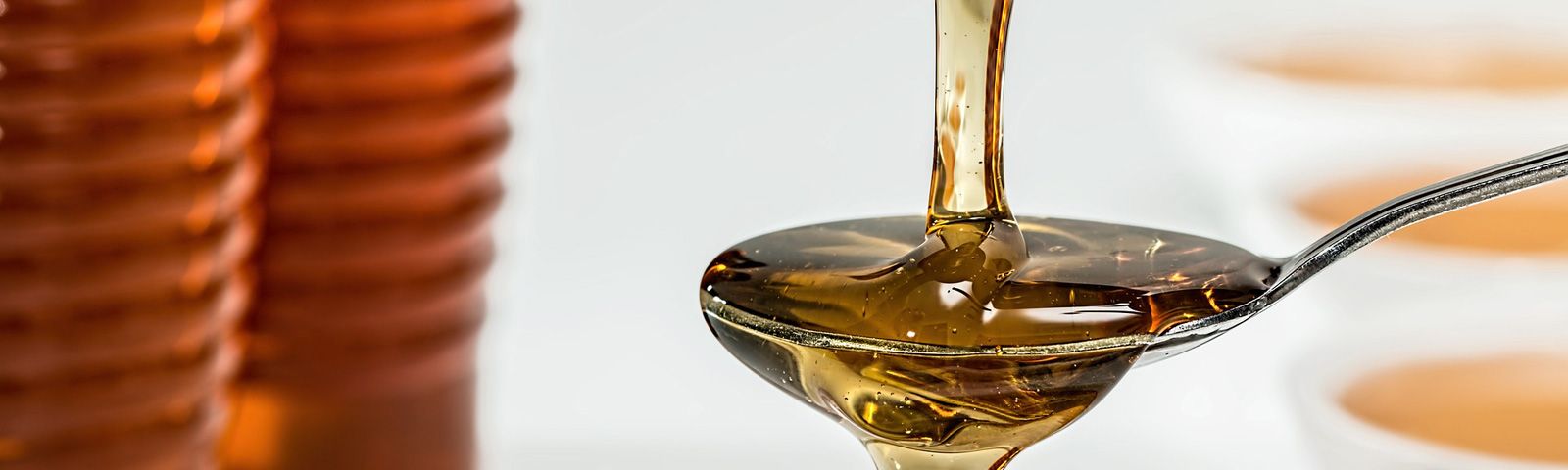 1707-honing-is-net-zo-ongez Sirup auf einem Löffel, vor einem unscharfen Hintergrund, der eine Ernährung für Fitnesskunden symbolisiert.