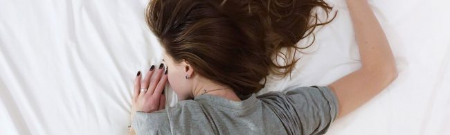 Frau schläft auf einem Bett, umgeben von weißer Bettwäsche.