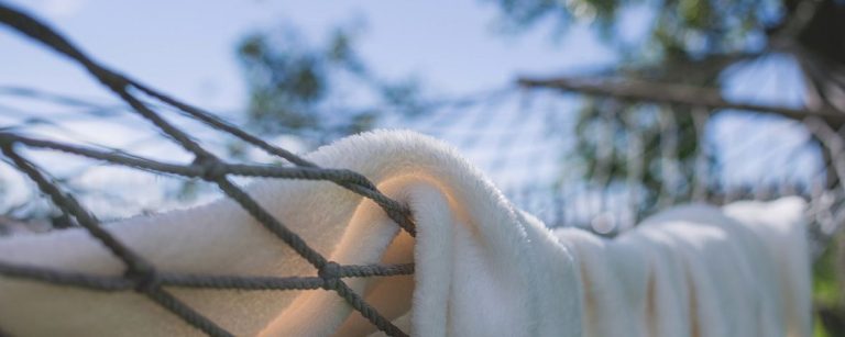 Weißes, flauschiges Handtuch in einer Hängematte, im Hintergrund verschwommene Bäume und blauer Himmel – ideal für Sportler.