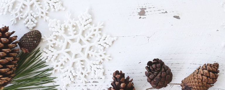 Weihnachtliche Dekoration mit Tannenzapfen und Schneeflocken auf weißem Holzhintergrund.