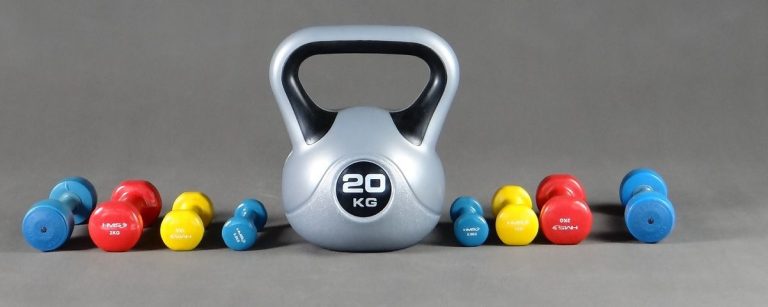Ein großer silberner Kettlebell mit 20 kg Gewicht, umgeben von bunten Kurzhanteln in Rot, Gelb und Blau.