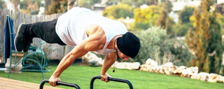 Mann macht Handstand-Liegestütze auf Parallettes im Freien.