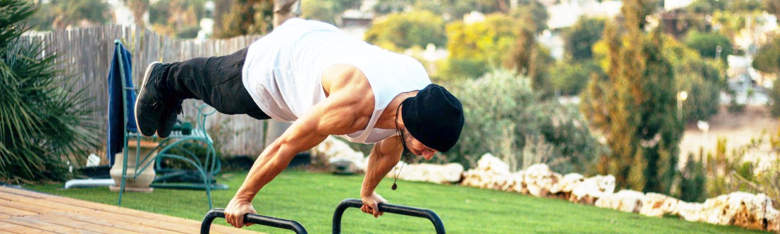 Mann macht Handstand-Liegestütze auf Parallettes im Freien.