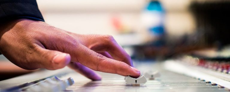 Hand, die einen Schieberegler auf einem Mischpult bedient, Aufnahme und Bearbeitung von Fitness-Ernährungs-Audio.