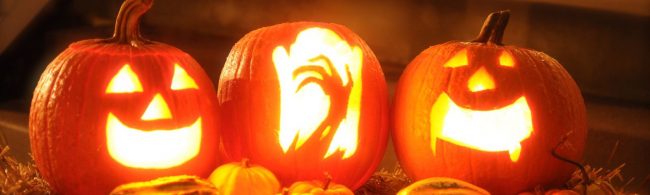 Beleuchtete Halloween-Kürbisse mit Gesichtern und kleineren Kürbissen im Vordergrund.