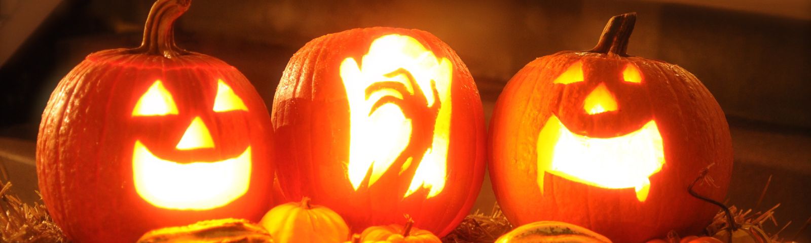 Beleuchtete Halloween-Kürbisse mit Gesichtern und kleineren Kürbissen im Vordergrund.