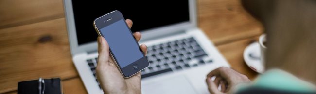 Person hält Smartphone vor Laptop. Fitness-Ernährungs-Firma.