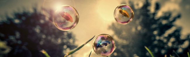 Sechs bunte Regenschirme schweben in Wasserblasen über saftigem Gras.