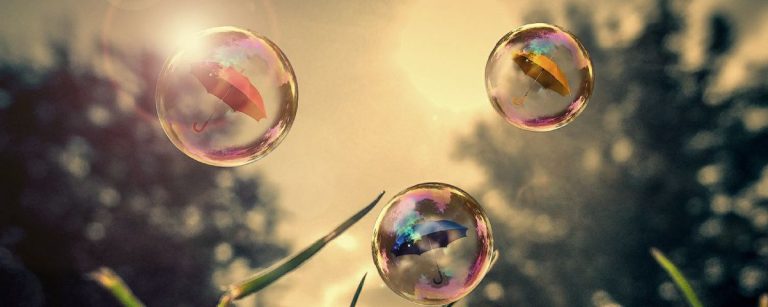 Sechs bunte Regenschirme schweben in Wasserblasen über saftigem Gras.