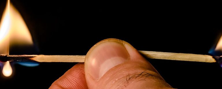 Zwei brennende Streichhölzer, die von einer Hand gehalten werden, symbolisieren Energie und Ausdauer.