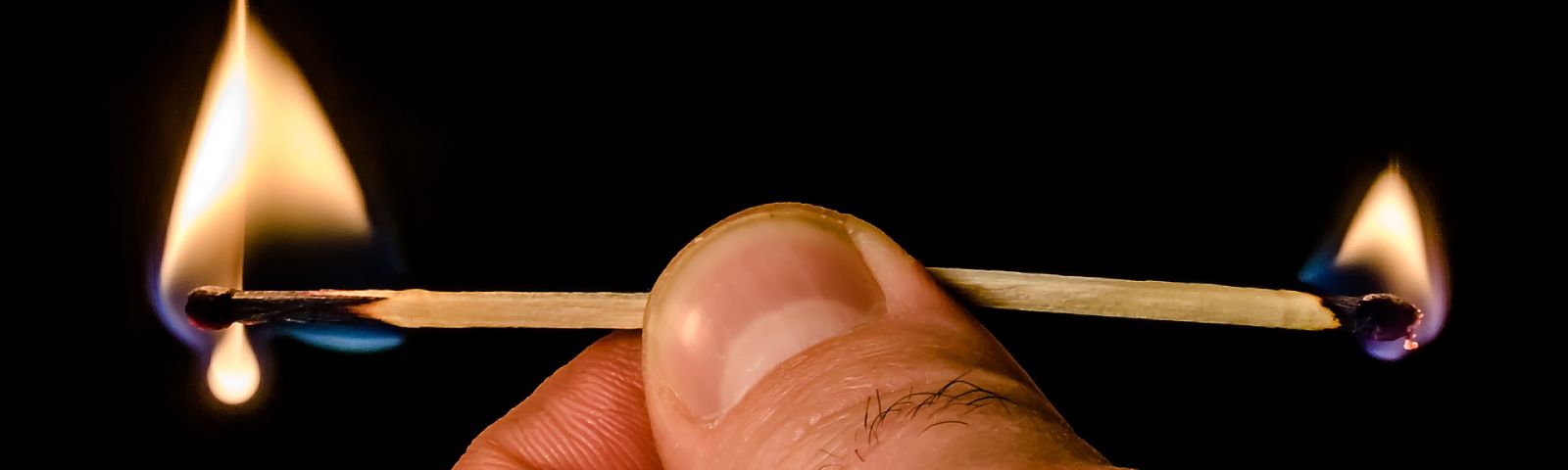 Zwei brennende Streichhölzer, die von einer Hand gehalten werden, symbolisieren Energie und Ausdauer.