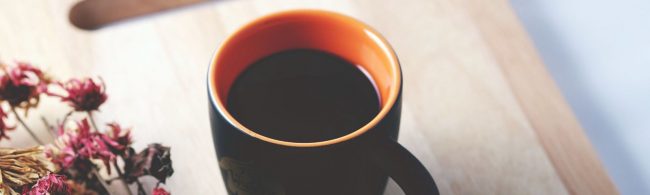 Gesunder Kaffee neben getrockneten Blumen auf Holzunterlage.