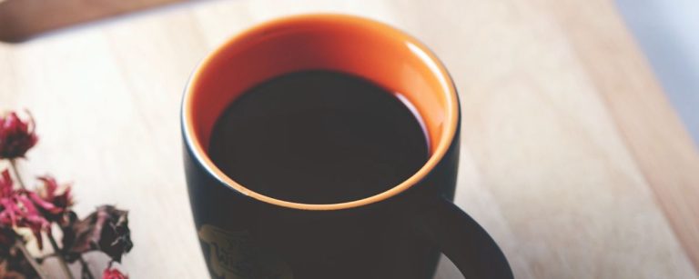 Gesunder Kaffee neben getrockneten Blumen auf Holzunterlage.