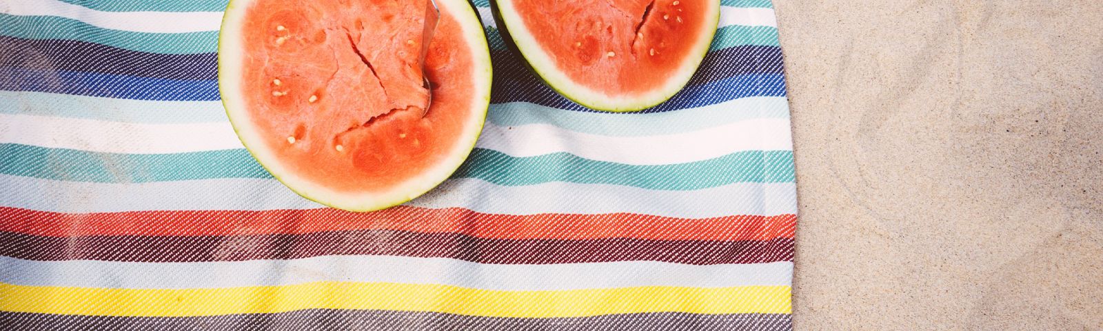 Zwei Wassermelonen auf einem gestreiften Handtuch am Strand – perfekt für eine gesunde Fitness-Ernährung.