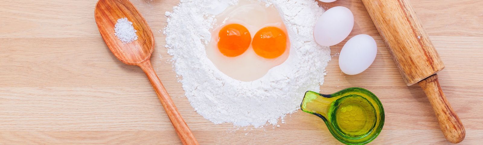 Zutaten für Fitness-Backen: Mehl, Eier, Öl und Salz auf Holzbrett.