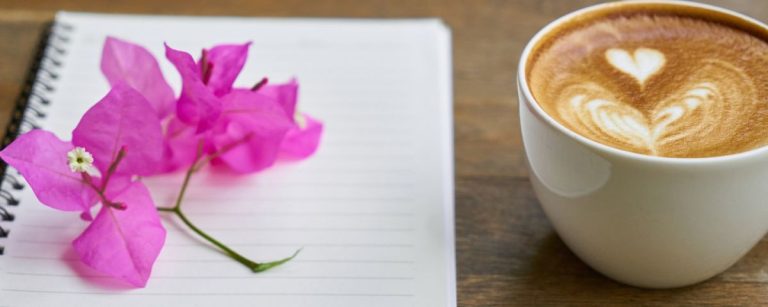 Latte Art Kaffee und pinke Blume auf Notizbuch für Fitness-Ernährung