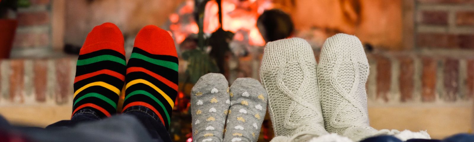 BF-onspannen-feestdagen-1600×480 Gemütliche Füße in Stricksocken am Kaminfeuer, perfekt für die Erholung nach dem Training.