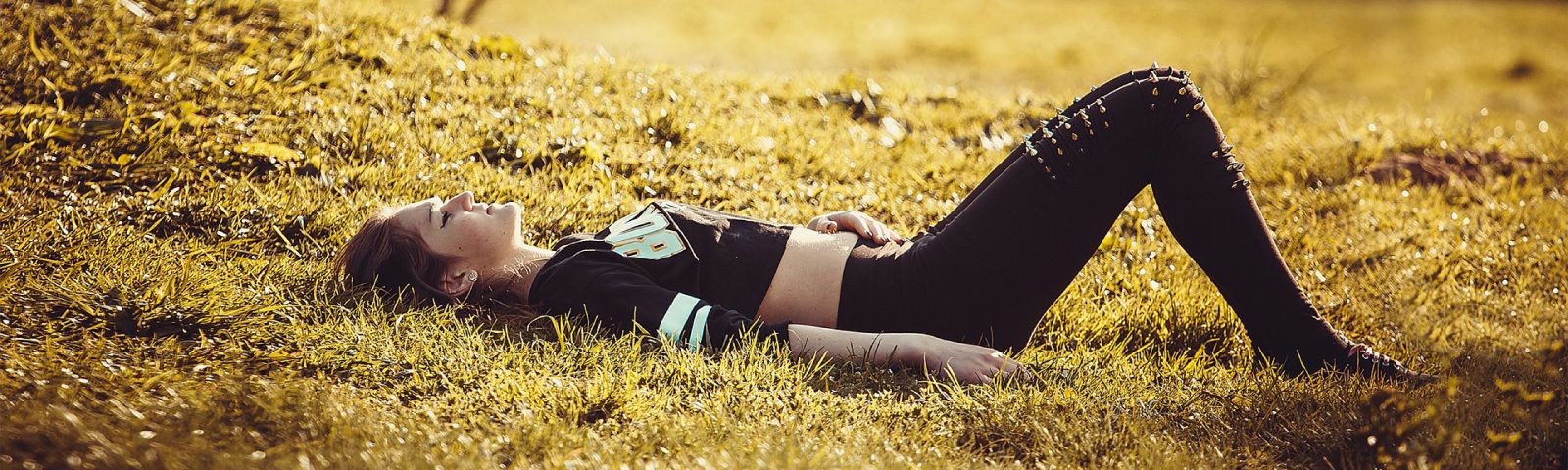 BF-pijn-1600×480 Junge Frau liegt auf sonnenbeschienener Wiese und entspannt sich, perfekt für Fitness und Ernährung.