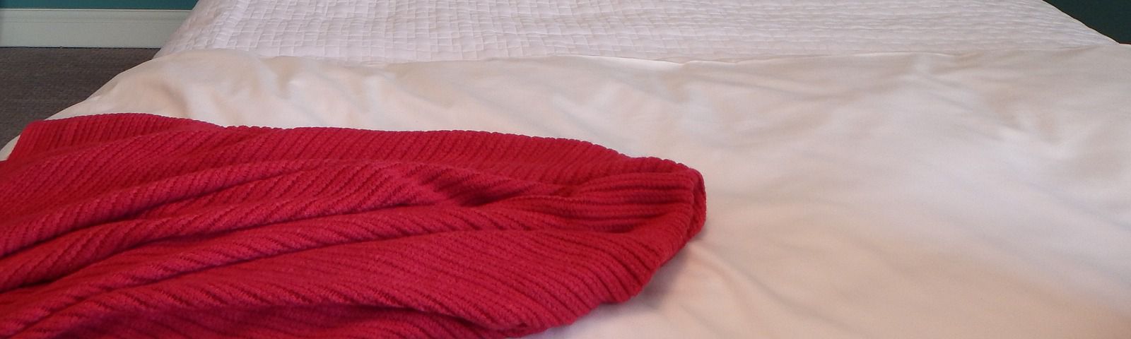 Rote Strickdecke auf einem weißen Bett, ideal für ein gemütliches Zuhause nach dem Training.