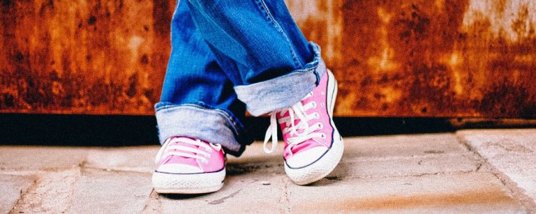 Person in Jeans und rosa Turnschuhen entspannt sich vor rostigem Hintergrund.