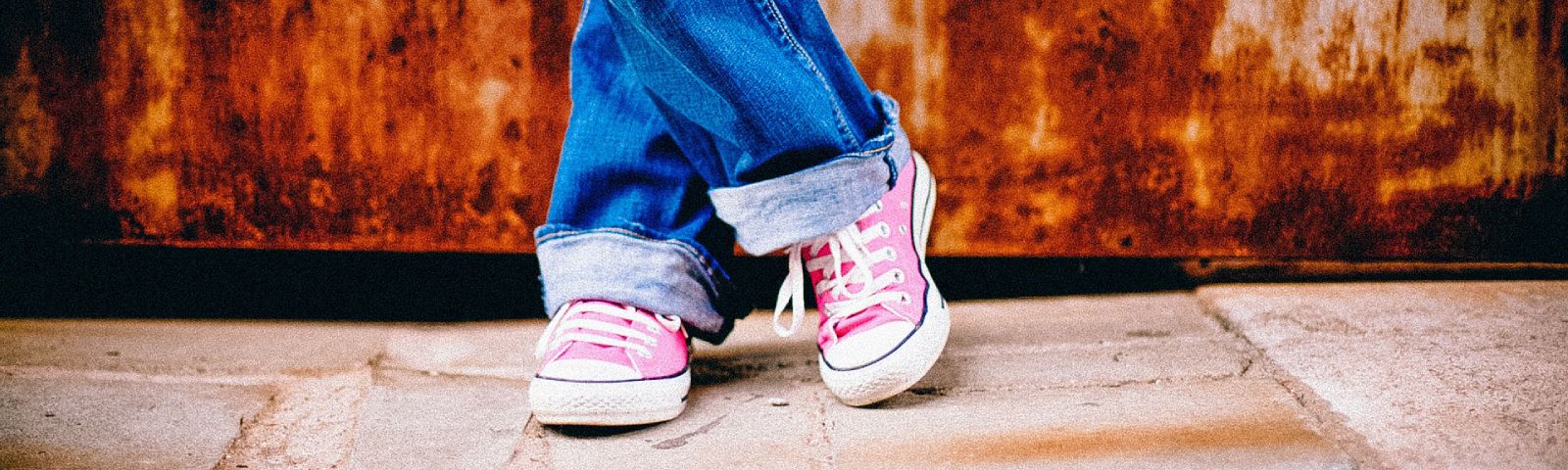 Person in Jeans und rosa Turnschuhen entspannt sich vor rostigem Hintergrund.