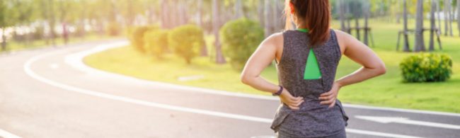 Frau mit Rückenschmerzen beim Laufen im Park. Ernährung für Sportler.