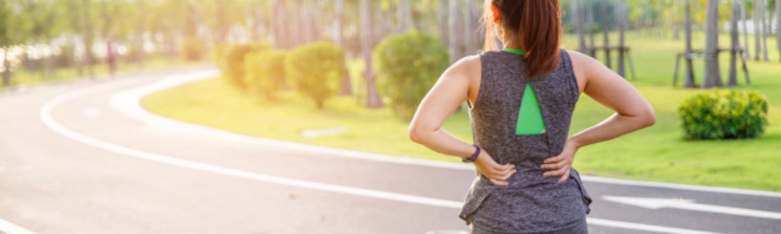 Frau mit Rückenschmerzen beim Laufen im Park. Ernährung für Sportler.