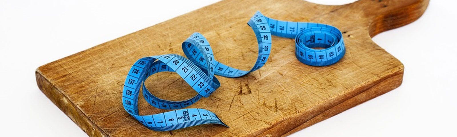 Blaues Maßband auf Holzbrett, symbolisiert Fitness und gesunde Ernährung.