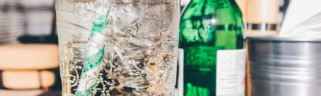 Kühles, sprudelndes Getränk mit Eis und Strohhalm neben einer grünen Flasche – perfekt für Fitness und Ernährung.