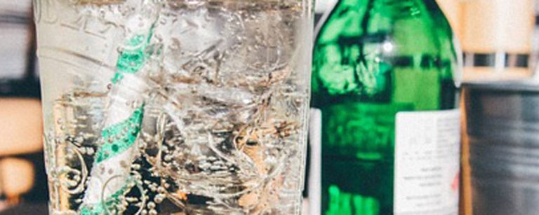 Kühles, sprudelndes Getränk mit Eis und Strohhalm neben einer grünen Flasche – perfekt für Fitness und Ernährung.