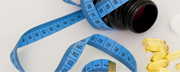 Blaues Maßband mit Pillen und Pillendose, symbolisiert Gewichtsverlust und gesunde Ernährung.