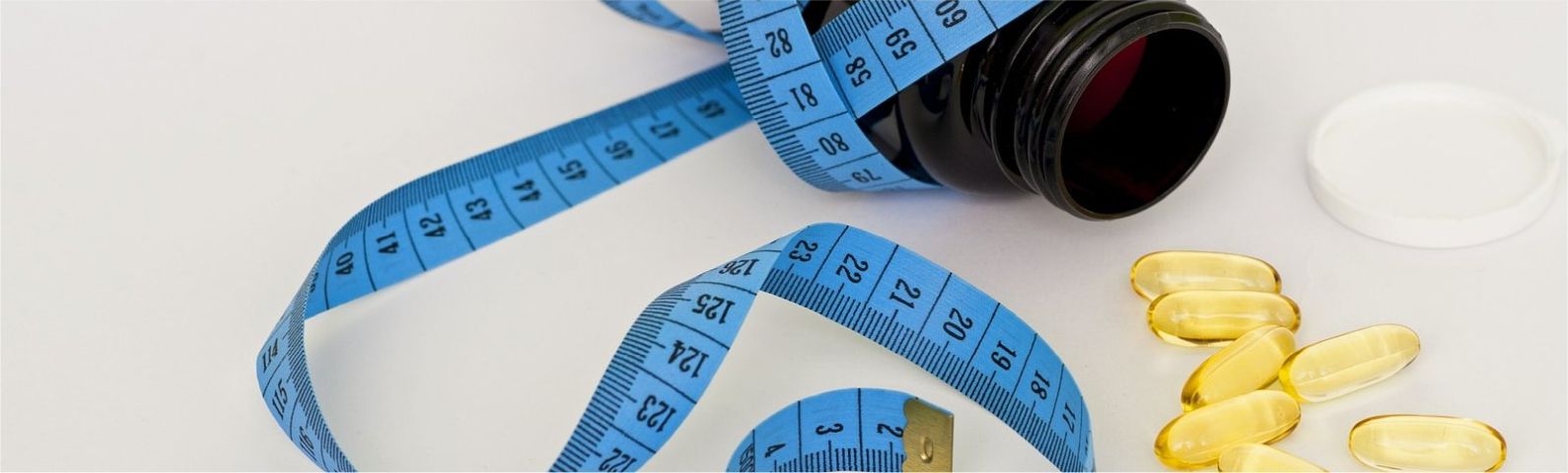 multi-groot Blaues Maßband mit Pillen und Pillendose, symbolisiert Gewichtsverlust und gesunde Ernährung.