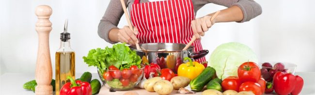 Person kocht gesundes Essen mit frischem Gemüse und Kräutern in einer Küche.