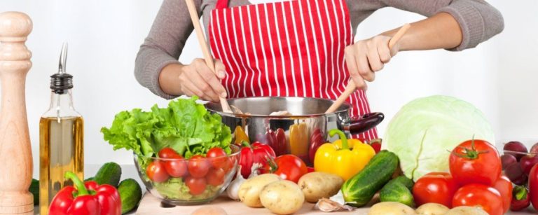 Person kocht gesundes Essen mit frischem Gemüse und Kräutern in einer Küche.