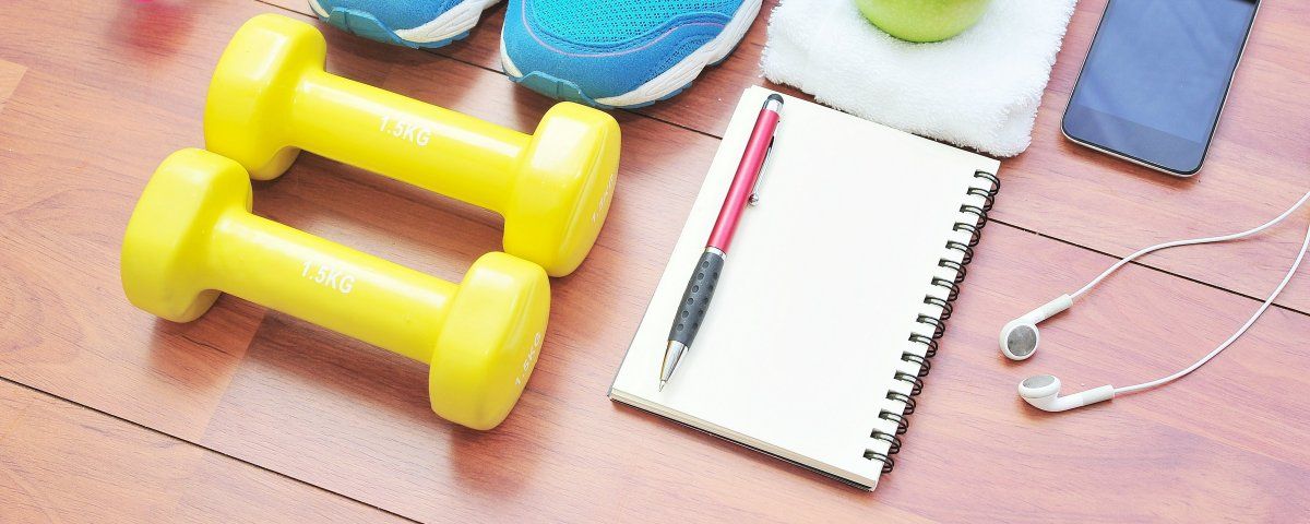 shutterstock-293243687groot Gelbe Kurzhanteln, Trainingsschuhe, Notizbuch, Stift, Kopfhörer, Handy, Apfel auf Handtuch.