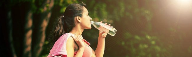 Junge Frau trinkt nach dem Sport Wasser in der Natur.