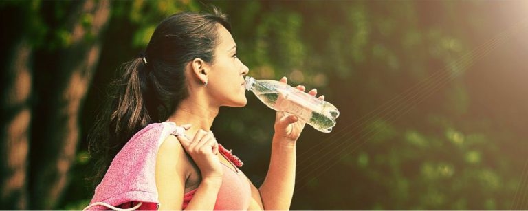 Junge Frau trinkt nach dem Sport Wasser in der Natur.