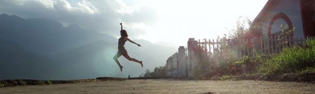 Junge Frau springt voller Energie im Freien mit Bergen im Hintergrund – Symbol für einen aktiven Lebensstil.