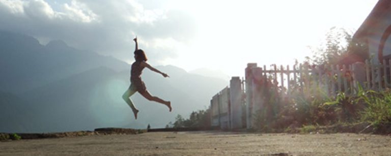 Junge Frau springt voller Energie im Freien mit Bergen im Hintergrund – Symbol für einen aktiven Lebensstil.