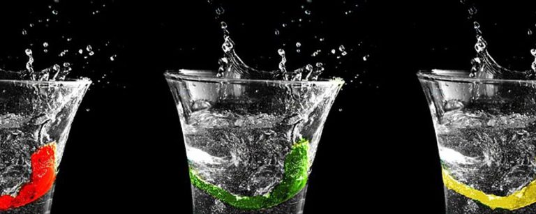 Gesunde Getränke mit Fruchtstücken: rote Beere, grüner Apfel und gelbe Zitrone in Wasserspritzern.