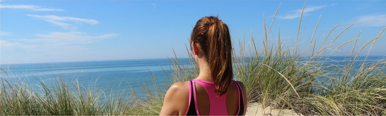 Frau mit Pferdeschwanz blickt aufs Meer, trainiert für gesunde Ernährung.