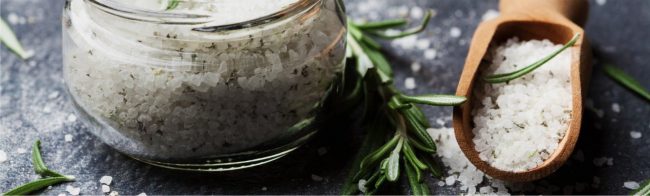 Grobes Salz mit Rosmarin in einem Glas und Holzlöffel für gesunde Ernährung.