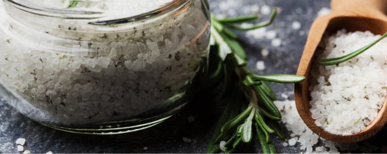 Grobes Salz mit Rosmarin in einem Glas und Holzlöffel für gesunde Ernährung.