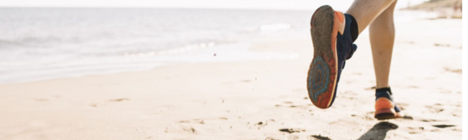 Ein Läufer in Turnschuhen und Shorts läuft am Strand entlang, um fit zu bleiben.