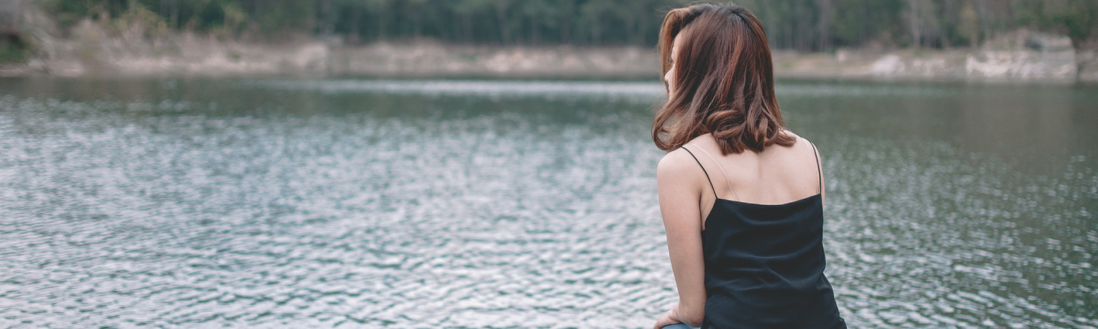 Junge Frau sitzt am Wasser in schwarzem Top.