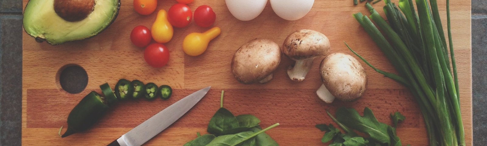 Schnittlauch, Pilze, Tomaten, Avocado, Jalapenos und Eier auf einem Holzbrett – Zutaten für gesunde Fitness-Mahlzeiten.