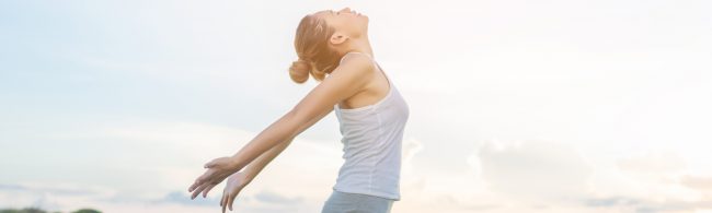 Frau mit ausgebreiteten Armen atmet tief durch und genießt die frische Luft.